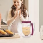 Batter dispenser filled with batter on a kitchen counter next to muffins
