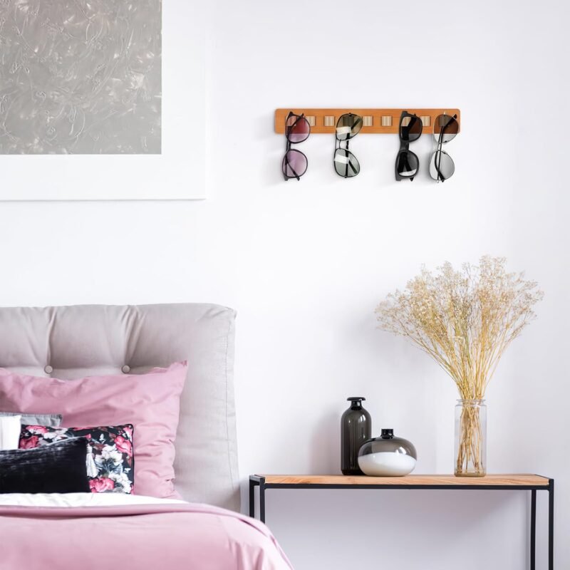 Bamboo glasses holder with leather straps mounted on a bedroom wall above a console table, holding four pairs of sunglasses