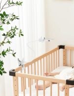 White flexible baby monitor holder clipped to a wooden cot in a nursery