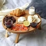 Round wooden picnic wine table with cheese and wine on a blanket