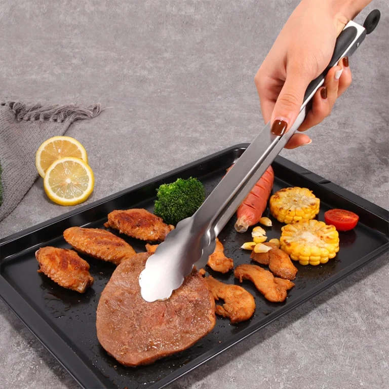 Stainless steel kitchen tongs serving food on a baking tray