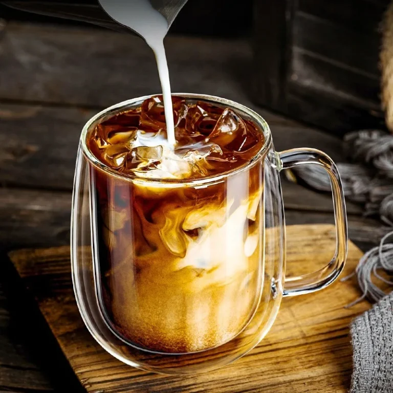 Double-walled glass mug with iced coffee on a wooden board
