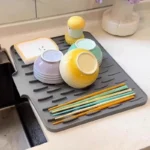 Grey silicone drain mat by the kitchen sink with bowls and chopsticks drying on it