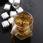 Stainless steel ice cubes next to a glass of whisky