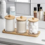 Three acrylic jars with wooden lids on a bamboo tray on a bathroom counter