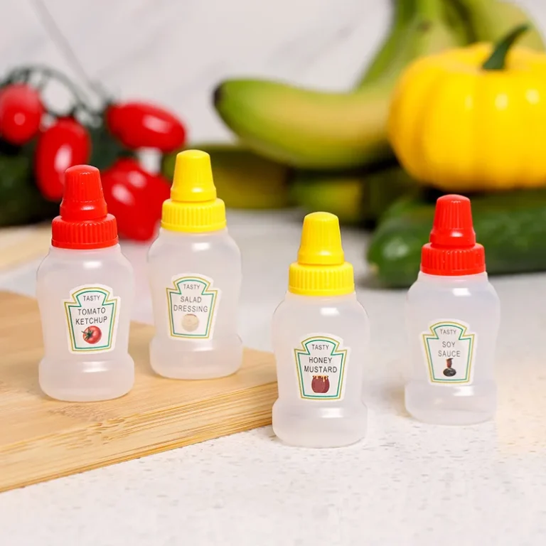 Four mini condiment squeeze bottles on a kitchen counter with fresh vegetables