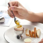 Stainless steel egg cup holding a soft-boiled egg on a breakfast plate with toast