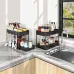 Two-tier black storage organiser holding spices and utensils on a kitchen worktop by the sink