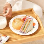 Triangular sandwich box on a breakfast tray with a bread roll and milk