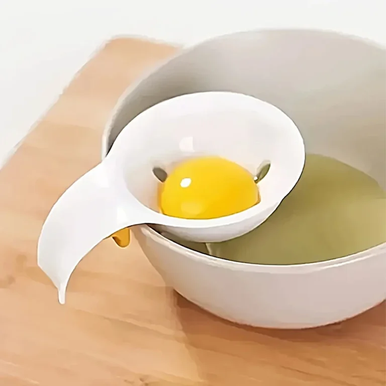 Egg separator holding a yolk over a bowl on a wooden chopping board
