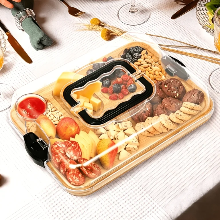 Bamboo serving board with clear lid and carry handle, filled with cheese, fruit and snacks on a dining table