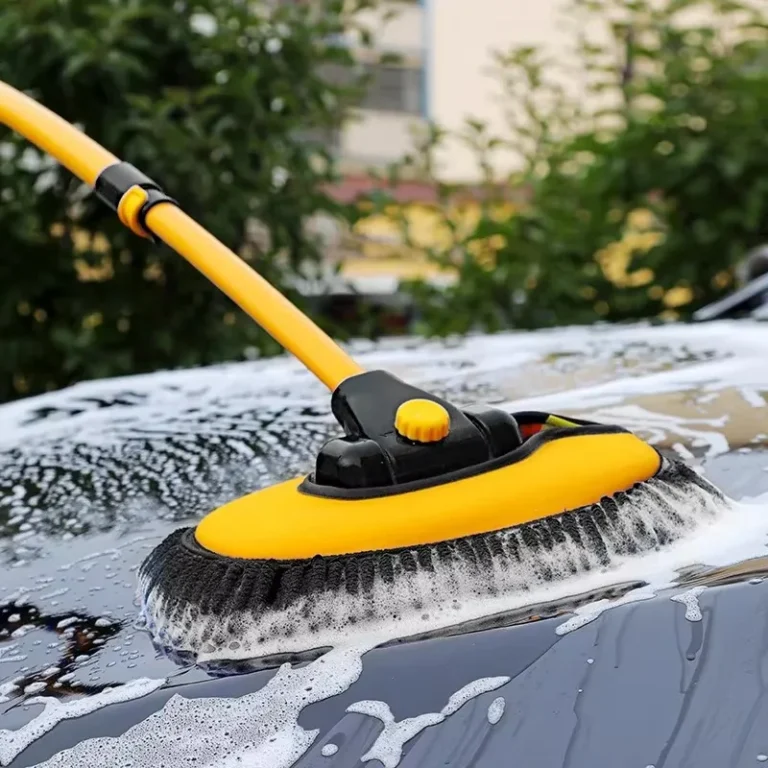 Car wash brush with telescopic handle washing a foamy car bonnet outdoors