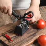 Red and black knife sharpener on a wooden board with scissors being sharpened