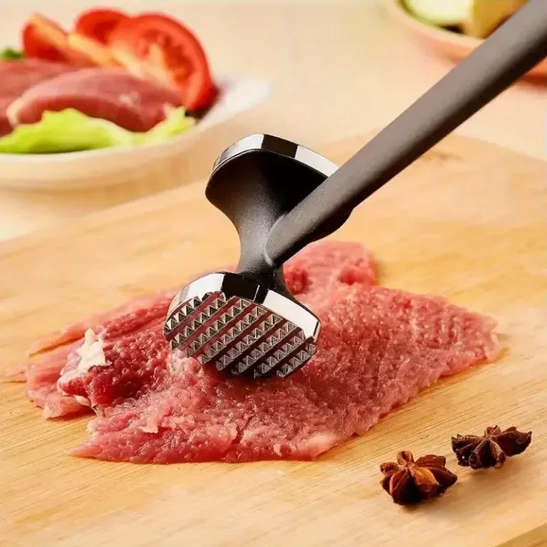 Meat tenderiser hammer on raw meat on a wooden chopping board
