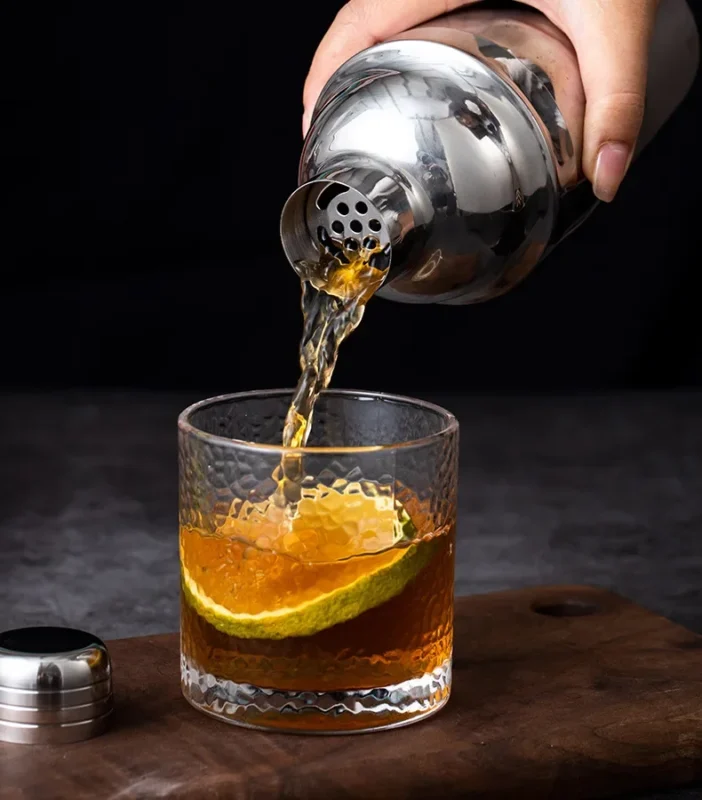 Stainless steel cocktail shaker pouring a drink over ice