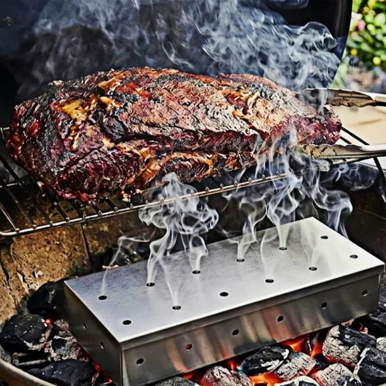 Perforated stainless steel smoker box on hot coals under a smoking joint of meat
