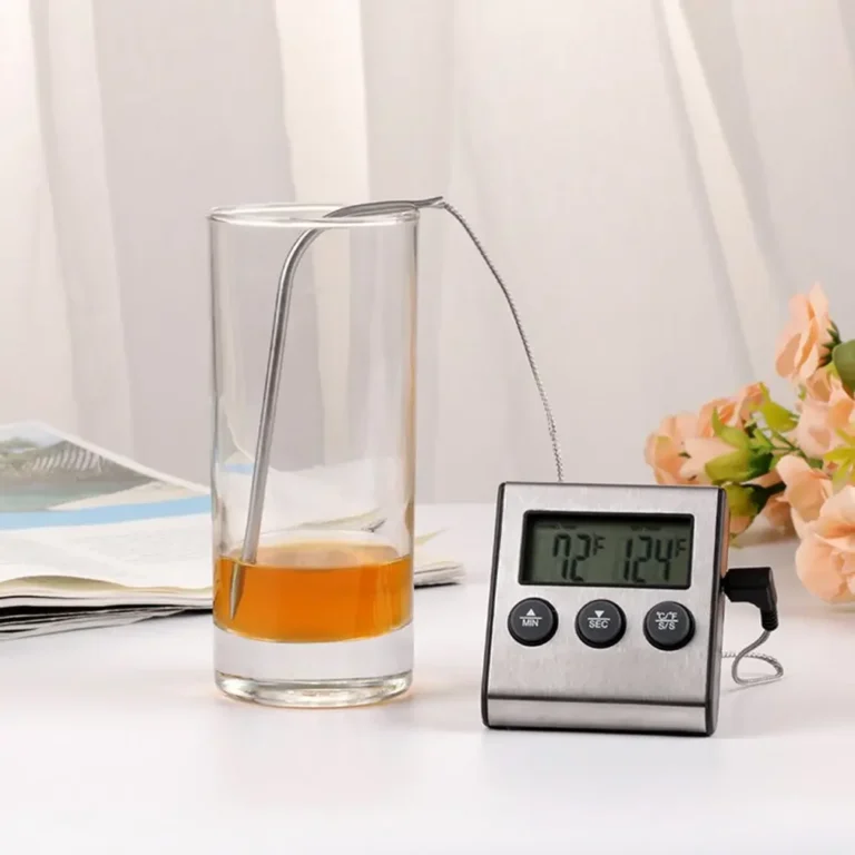 Digital thermometer with probe in a glass on a table with flowers