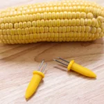 Yellow corn cob holder on a wooden table next to corn on the cob
