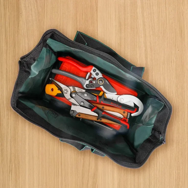 Green tool bag open with garden tools inside on a wooden floor