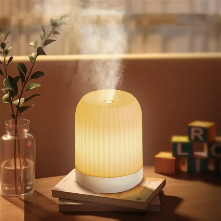 Glowing aroma diffuser releasing mist on a stack of books beside a vase