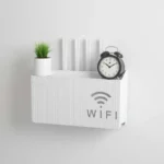 White wall-mounted router storage box with WiFi print, holding a plant and alarm clock